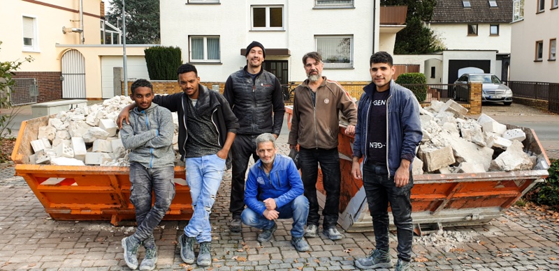 Sechs Bewohner und Aktive der CFEE posieren vor zwei Containern, die mit Bauschutt gefüllt sind.