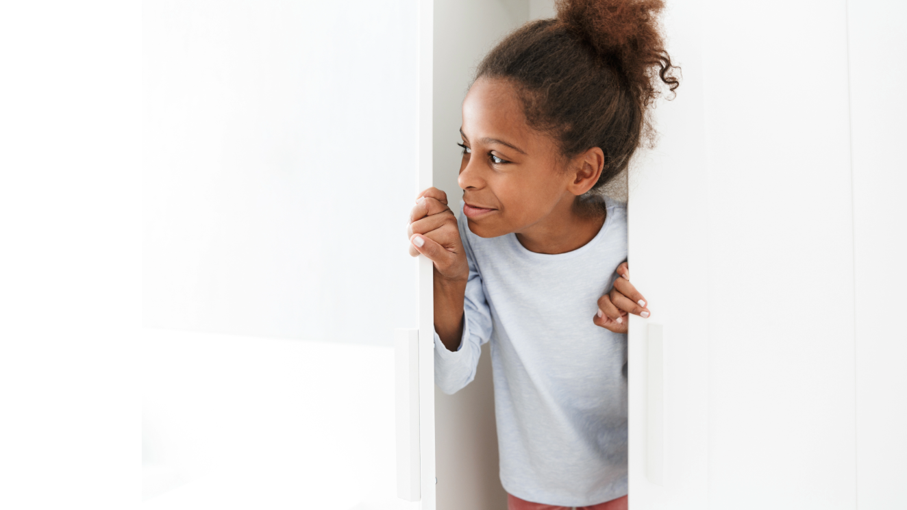 Mädchen schaut vorsichtig und neugiereig durch eine WOhnungstür