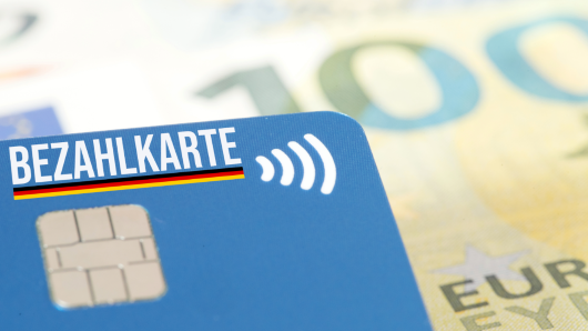 Geldkarte mit der Aufschrift "Bezahlkarte" vor dem Hintergrund eines 100-Euro-Scheins